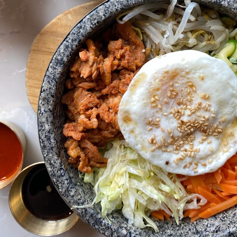 Close-up of a Korean bibimbap bowl with spicy pork, fried egg, bean sprouts, and carrots.