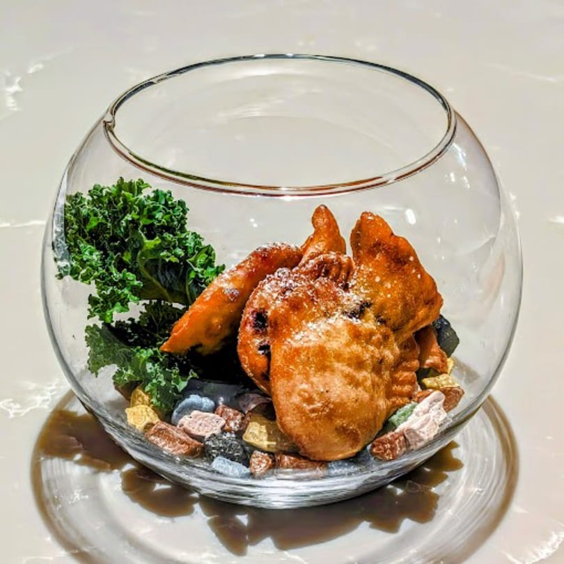 Korean fried dessert, possibly yakgwa, dusted with powdered sugar and garnished with kale in a glass bowl.
